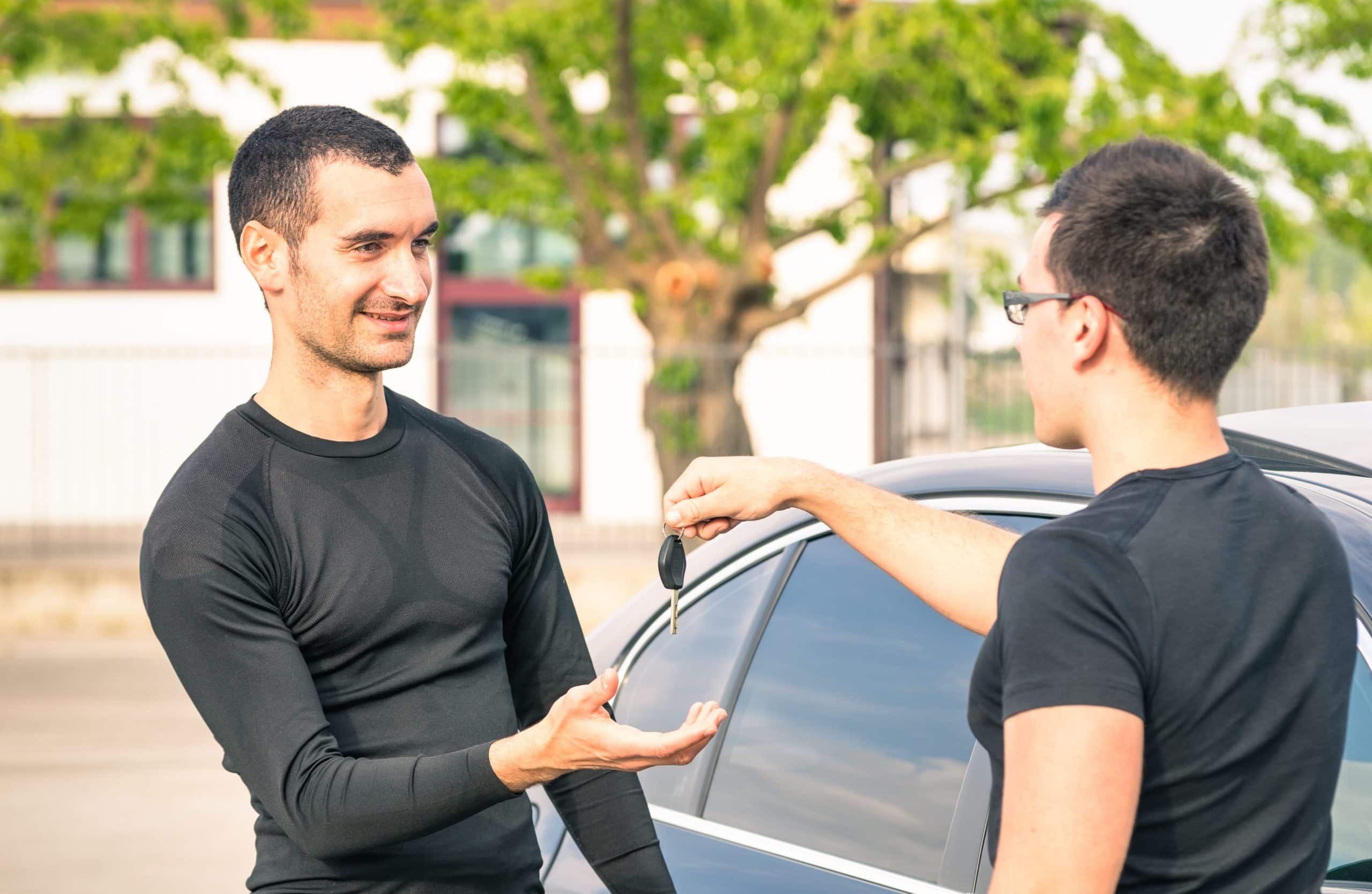 Man Handing Off Car Keys To Other Young Man After Selling