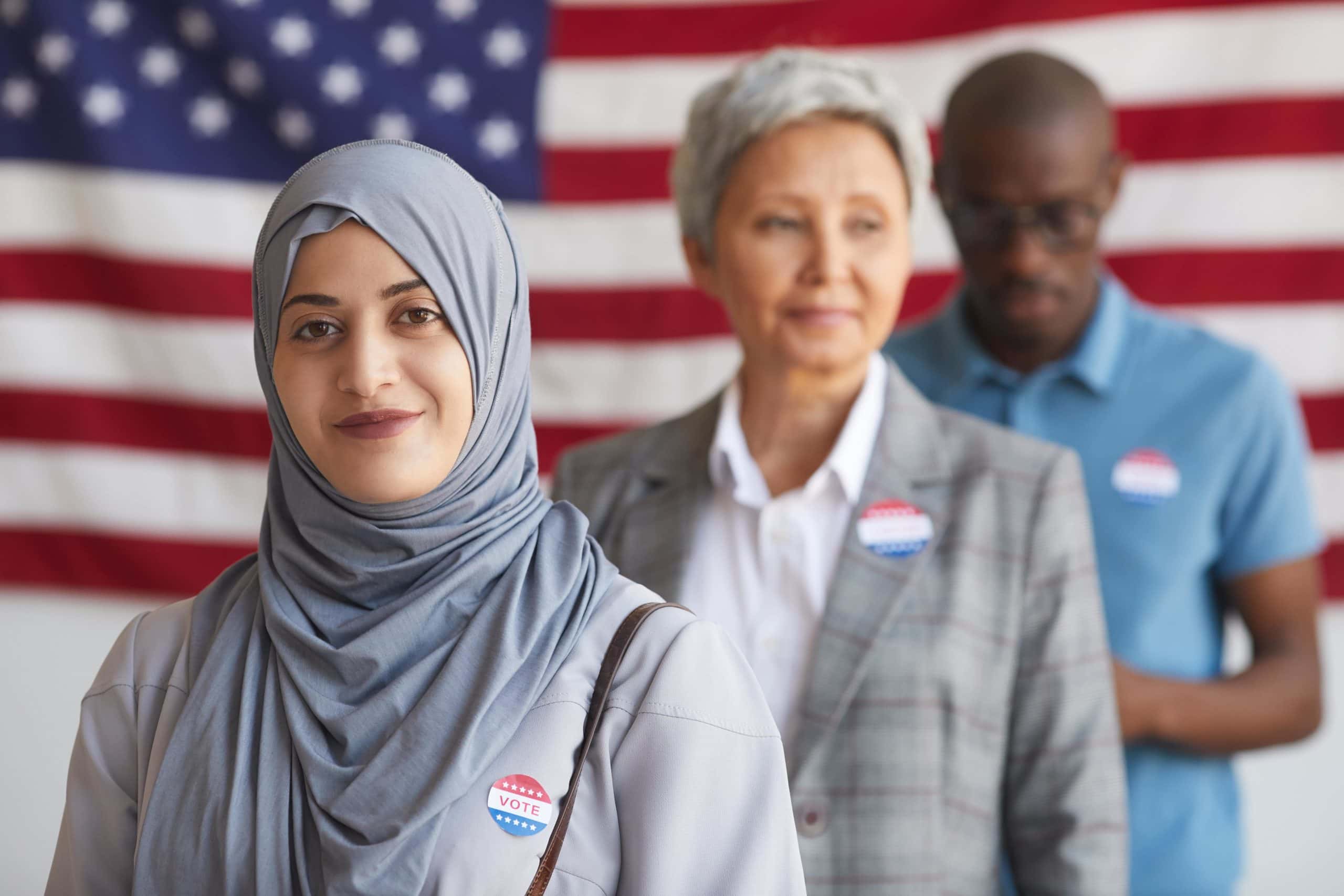 Woman In Hijab Standing In Front Of Older Woman And Black Man Wearing Vote Stickers